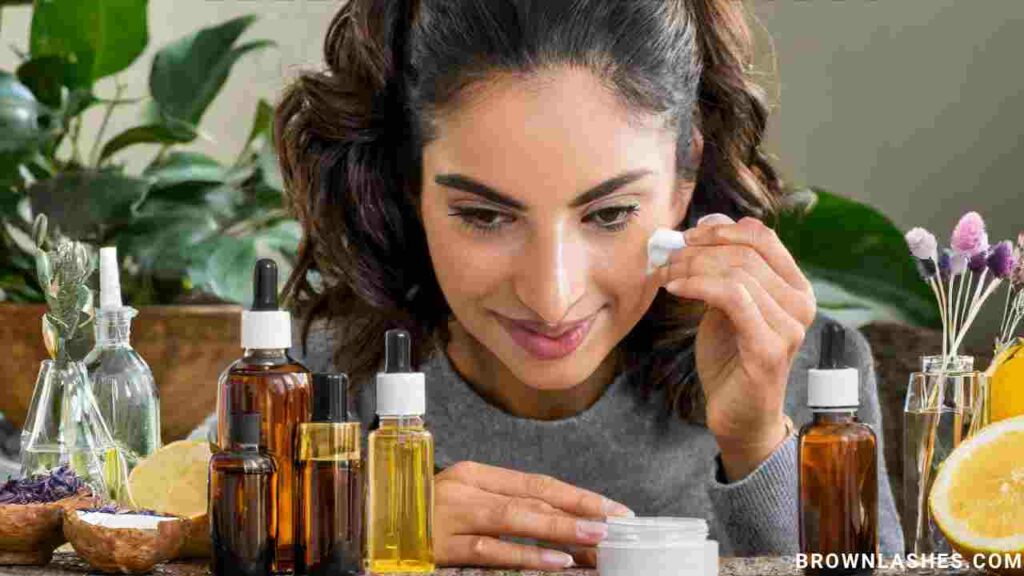 A woman applying a homemade lash conditioner using a small brush, surrounded by bottles of natural oils.