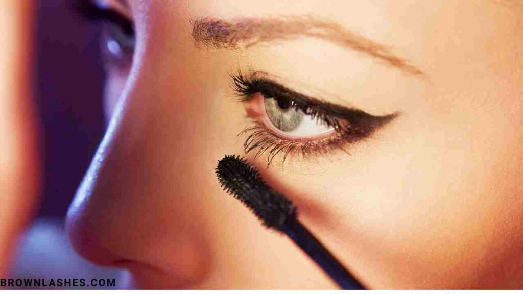 A close-up of a woman gently brushing her natural eyelashes with a clean mascara wand to prevent breakage.