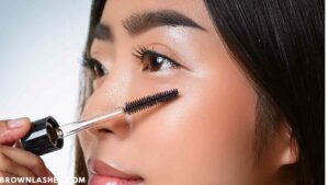 A person holding a spoolie brush and gently brushing their eyelashes to stimulate growth and improve lash health.